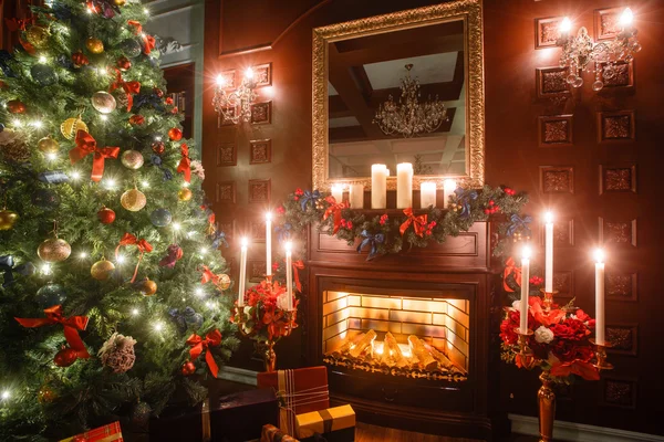 Noel akşam mum ışığında. Klasik dairelerde beyaz bir şömine, dekore edilmiş ağaç, kanepe, büyük pencereler ve avize. — Stok fotoğraf
