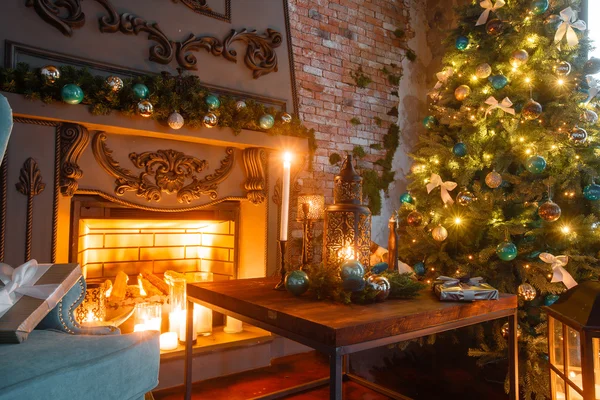 Noche de Navidad a la luz de las velas. apartamentos clásicos con chimenea blanca, árbol decorado, sofá, grandes ventanales y lámpara de araña . —  Fotos de Stock