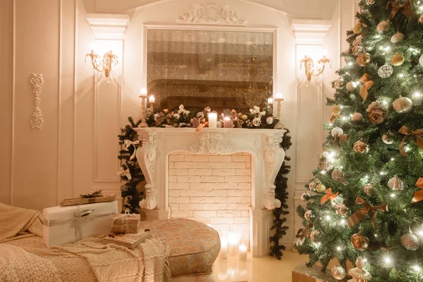 Jul på kvällen med levande ljus. klassiska lägenheter med stora fönster, ljusa soffa, dekorerade träd, en vit spis — Stockfoto