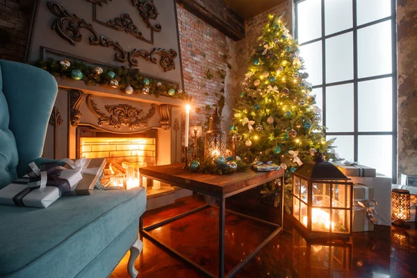 Jul på kvällen med levande ljus. klassiska lägenheter med en vit spis, dekorerade träd, soffa, stora fönster och ljuskrona. — Stockfoto