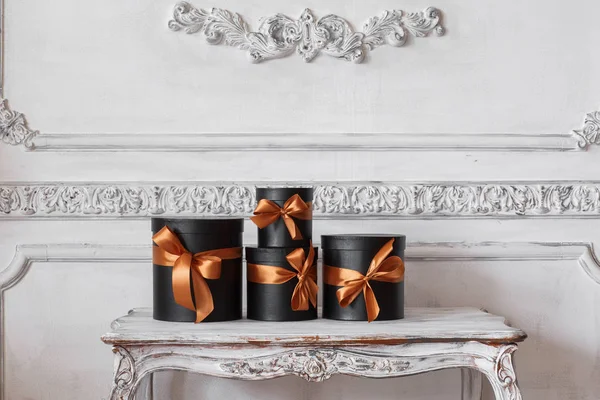 Загорнуті подарункові чорні коробки зі стрічками як різдвяні подарунки на столі Розкішний дизайн білої стіни барельєфні ліпнини рококо елементи — стокове фото