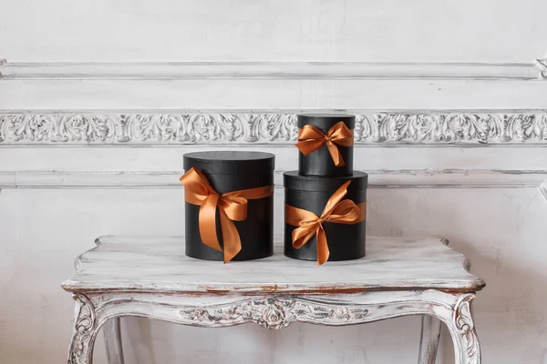 Загорнуті подарункові чорні коробки зі стрічками як різдвяні подарунки на столі Розкішний дизайн білої стіни барельєфні ліпнини рококо елементи — стокове фото