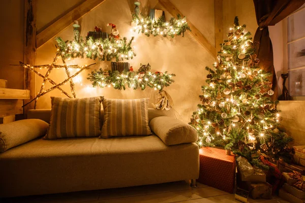 Imagen tranquila del interior de la casa moderna sala de estar decorado árbol de Navidad y regalos, sofá, mesa cubierta con manta . — Foto de Stock