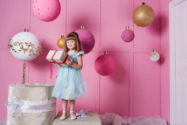 Pretty girl child 4 years old in a blue dress. Baby holding gift in their hands. Rose quartz room decorated holiday — Stock Photo, Image