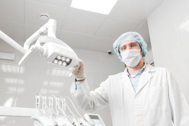 Yüzünde, gözlük, lamba elinde tutan bir doktor portre dişçi, cerrah üniforma ve maske alanlarındaki alt görünümü.
