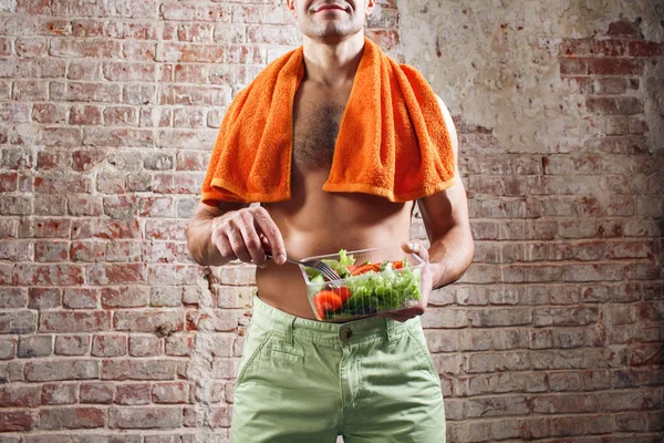 Fit man holding a bowl of fresh salad on old red bricks background