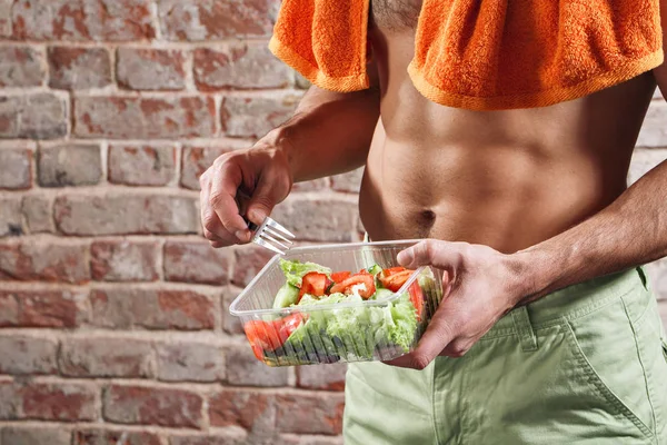 Fit man holding a bowl of fresh salad on old red bricks background
