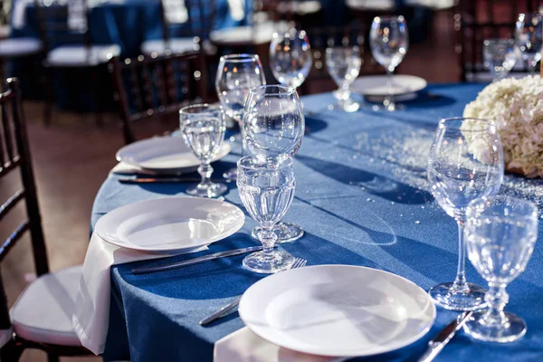 Boda. Banquete. Las sillas y la mesa redonda para los huéspedes, servidas con cubiertos y vajilla y cubiertas con un mantel azul . — Foto de Stock