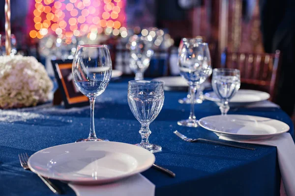 Boda. Banquete. Las sillas y la mesa redonda para los huéspedes, servidas con cubiertos y vajilla y cubiertas con un mantel azul . — Foto de Stock