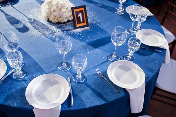 Boda. Banquete. Las sillas y la mesa redonda para los huéspedes, servidas con cubiertos y vajilla y cubiertas con un mantel azul . — Foto de Stock
