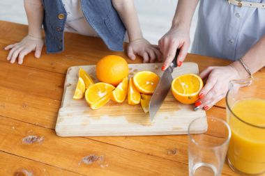 Anne oğluna meyve keser. dilimlenmiş portakal ahşap kesme tahtası üzerinde. Sağlıklı ve lezzetli kahvaltı