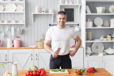 Orta yaşlı atlet, sebze salata salatalık ve domates keser. Vejetaryen yiyecekler