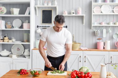 Orta yaşlı atlet, sebze salata salatalık ve domates keser. Vejetaryen yiyecekler