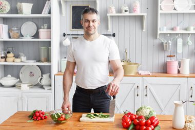Orta yaşlı atlet, sebze salata salatalık ve domates keser. Vejetaryen yiyecekler