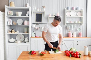Orta yaşlı atlet, sebze salata salatalık ve domates keser. Vejetaryen yiyecekler