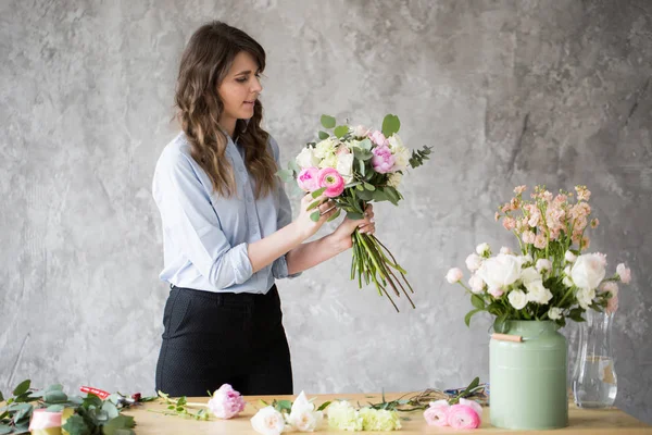 Florist at work: pretty young woman making fashion modern bouquet of different flowers