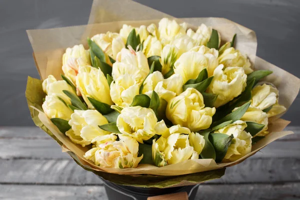Tulipes de couleurs pastel jaune doux dans un vase sur une table en bois. Mur gris — Photo