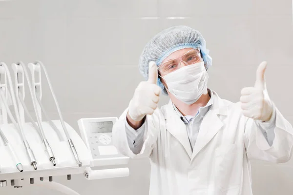 Retrato del dentista masculino feliz usando bata de laboratorio mientras está sentado en la clínica — Foto de Stock