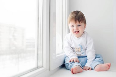 Pencere kenarında oturma sevimli küçük bebek. kameraya bak
