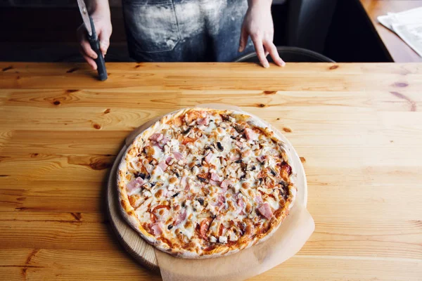 Großaufnahme Hand des Chefs Bäcker in Jeans einheitliche Schürze schneidet Pizza in der Küche — Stockfoto
