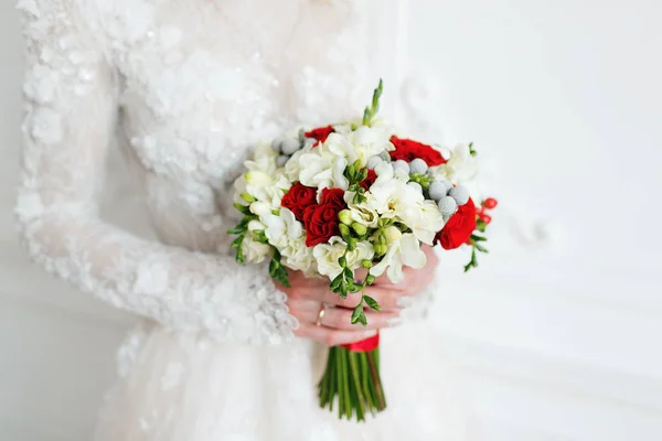 Невеста держит свадебный букет близко. красные и белые розы, фрезия, брюния, украшенные в композиции — стоковое фото