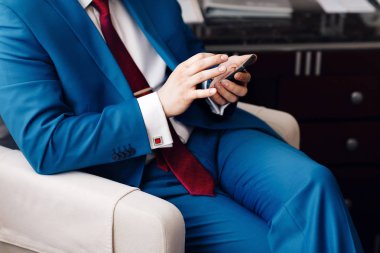 Bir telefon iş adamı tutmak elinde iken mavi elbiseli bir kanepede oturuyor. el pahalı mekanik saat üzerinde deri kayışı ile. kol düğmesi ile gömlek