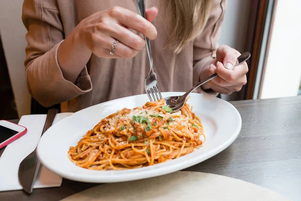 Girl eats Italian pasta with tomato, meat. Close-up spaghetti Bolognese wind it around a fork with a spoon. Parmesan cheese — Stock Photo, Image