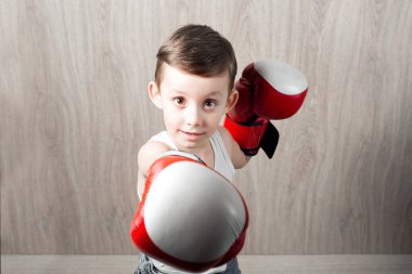 Boks eldivenleri büyüklüğü ile şirin küçük çocuk. Sportif bir çocuk portresi kutusunda meşgul. çevresinde ve ciddi değil şaka. ahşap arka plan