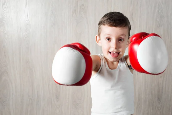 Netter kleiner Junge mit großen Boxhandschuhen. Porträt eines sportlichen Kindes, das sich in der Box engagiert. Herumalbern und nicht ernst nehmen. hölzerner Hintergrund — Stockfoto
