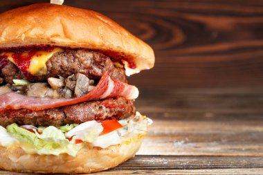 Ev Close-Up sığır eti, mantar, sosis ve peynir ile lezzetli hamburger ahşap masanın üzerine yaptı. Kızılcık acı sos.