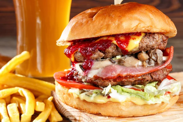 El primer plano de la casa hizo sabrosas hamburguesas con carne de res, champiñones, tocino y queso en la mesa de madera. salsa picante de arándano. cerveza y patatas fritas — Foto de Stock