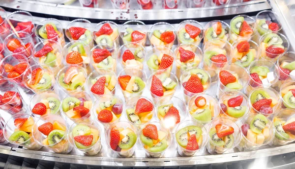 Ensalada de frutas arreglada en vasos de plástico para la venta. escaparate refrigerador o buffet. Utilizado en cócteles y como relleno de la fuente de chocolate. Enfoque selectivo — Foto de Stock