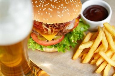 Büyük lezzetli hamburger ve patates kızartması ile ön plan ahşap masa üzerinde bira