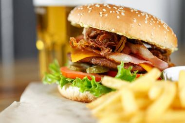 Büyük lezzetli hamburger ve patates kızartması artalanları ahşap masa üzerinde bira ile
