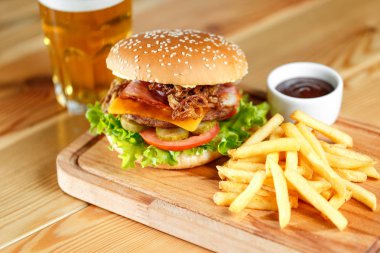 Büyük lezzetli hamburger ve patates kızartması artalanları ahşap masa üzerinde bira ile
