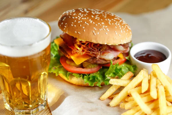 Hamburguesa grande y sabrosa y papas fritas con cerveza en primer plano en la mesa de madera — Foto de Stock