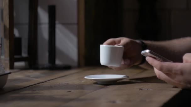 Homem senta-se com smartphone na mesa com xícara de café — Vídeo de Stock