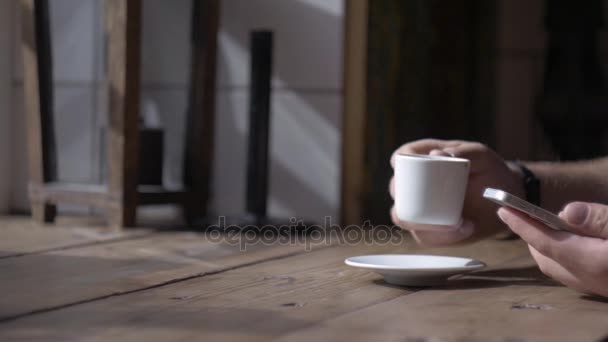 Homem senta-se com smartphone na mesa com xícara de café — Vídeo de Stock