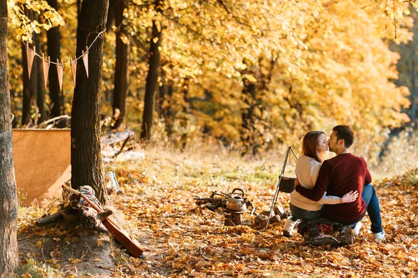 Acampamento outono. casal feliz abraçando e fazendo chá ou café. bebidas quentes . — Fotografia de Stock