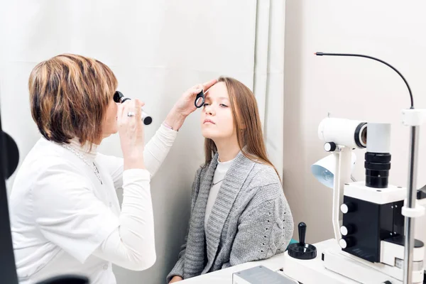 Optometrista femenina mayor examinando ojos de mujeres jóvenes en clínica privada — Foto de Stock