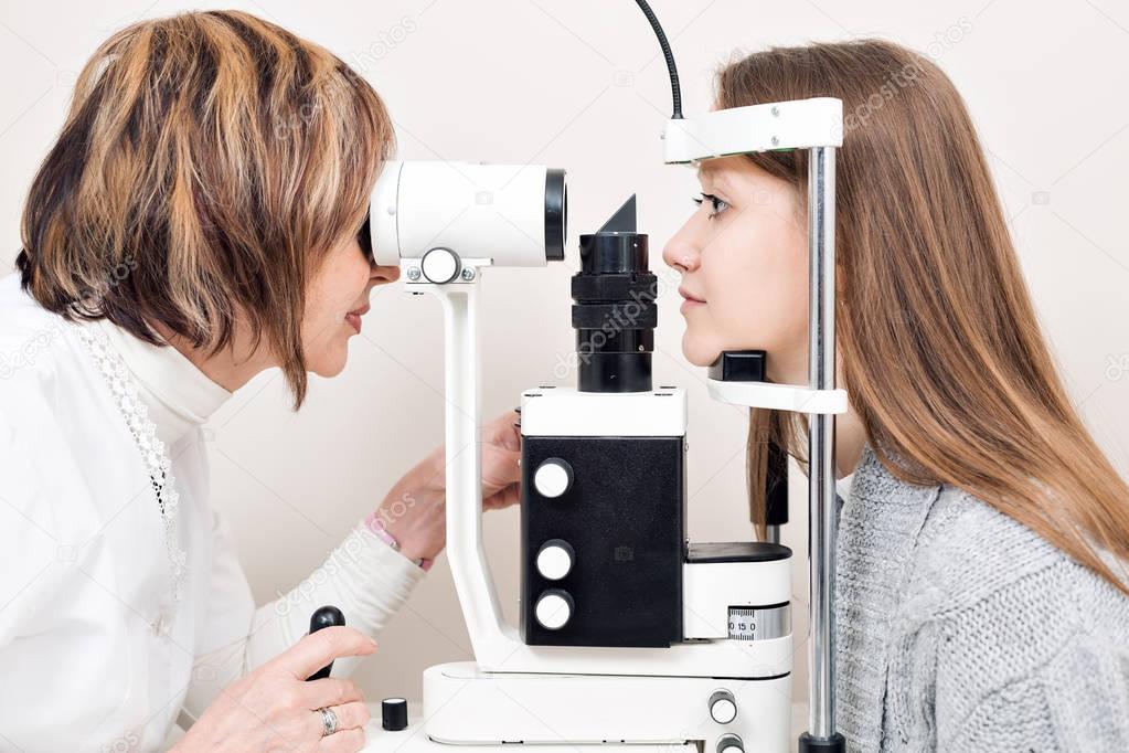 Senior female optometrist examining young womans eyes in private clinic