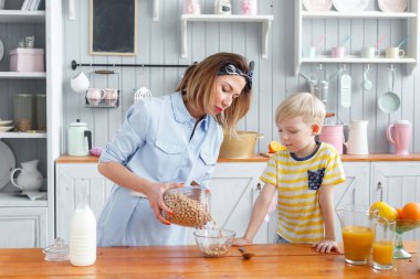 Anne ve oğul mutfakta bir kahvaltı yaparken gülümsüyorsun. Anne süt ve Mısır gevreği cam içine dökme
