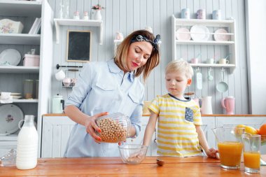 Anne ve oğul mutfakta bir kahvaltı yaparken gülümsüyorsun. Anne süt ve Mısır gevreği cam içine dökme