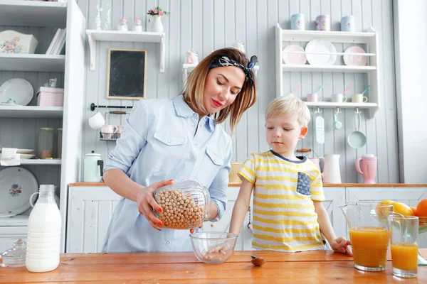 Anne ve oğul mutfakta bir kahvaltı yaparken gülümsüyorsun. Anne süt ve Mısır gevreği cam içine dökme