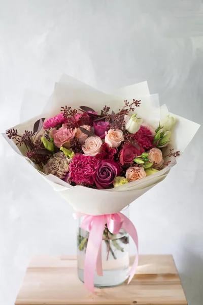 Composición floral con rosas y mezclar flores en jarrón de vidrio sobre un fondo gris . — Foto de Stock