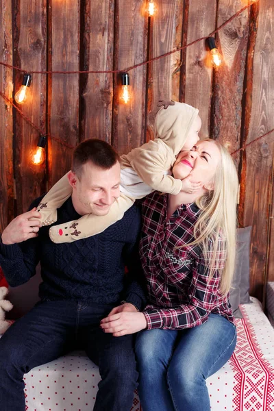 Happy family at Christmas. The parents and the baby sitting. Wall of wooden planks and garland — Stock Photo, Image