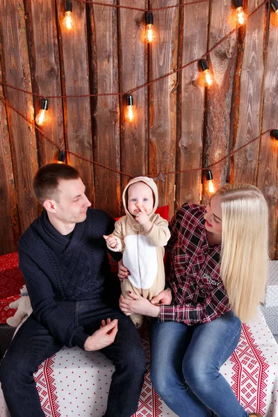 Noel mutlu bir aile. Anne ve bebek oturma. Duvar ahşap plakalar ve çelenk — Stok fotoğraf