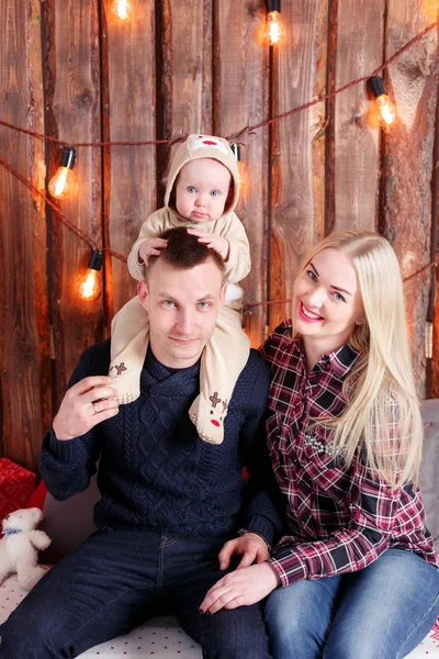 Happy family at Christmas. The parents and the baby sitting. Wall of wooden planks and garland — Stock Photo, Image