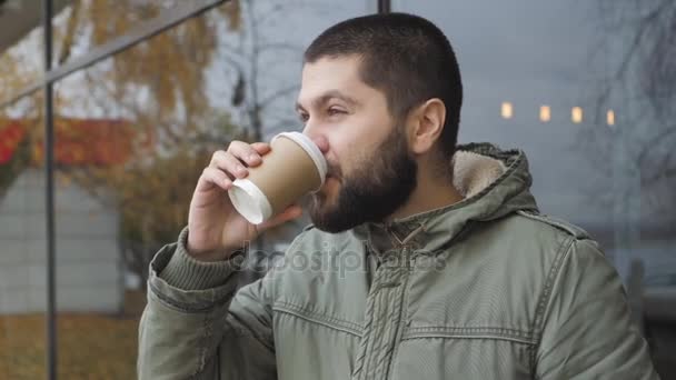 Knappe jonge bebaarde man houdt een kopje. warme drank koffie of thee drinken in de herfst buiten — Stockvideo