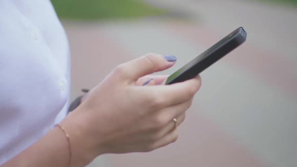 Vista lateral de un teléfono móvil de mensajería de texto de chica universitaria en el parque. primer plano — Vídeos de Stock